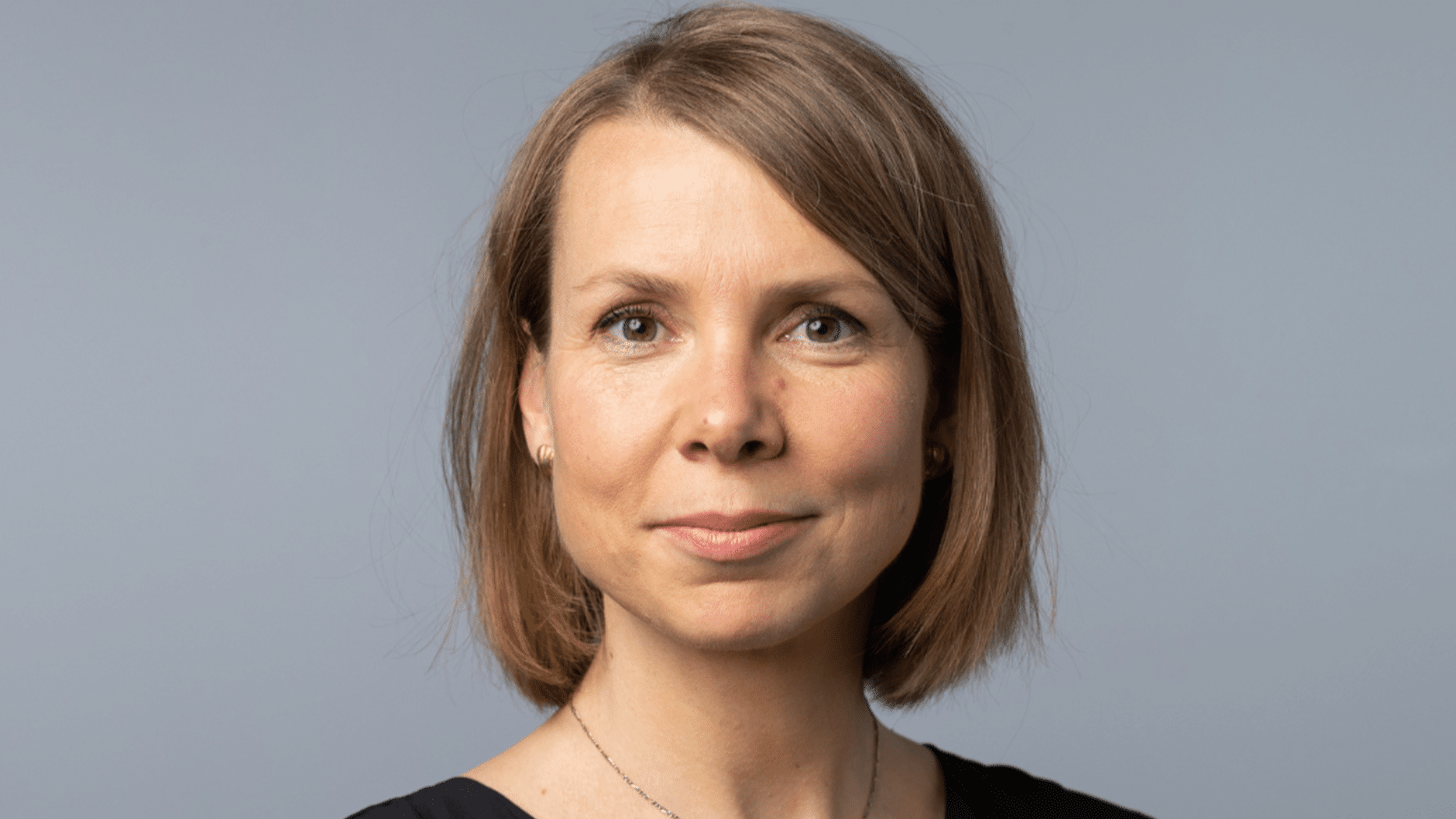 Porträt einer Frau mit kurzem, braunem Haar, neutralem Hintergrund, in schwarzem Oberteil, freundlicher Ausdruck.