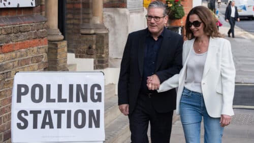 Keir Starmer und seine Frau Victoria gehen Hand in Hand zu einem Wahllokal mit einem Schild "Polling Station".