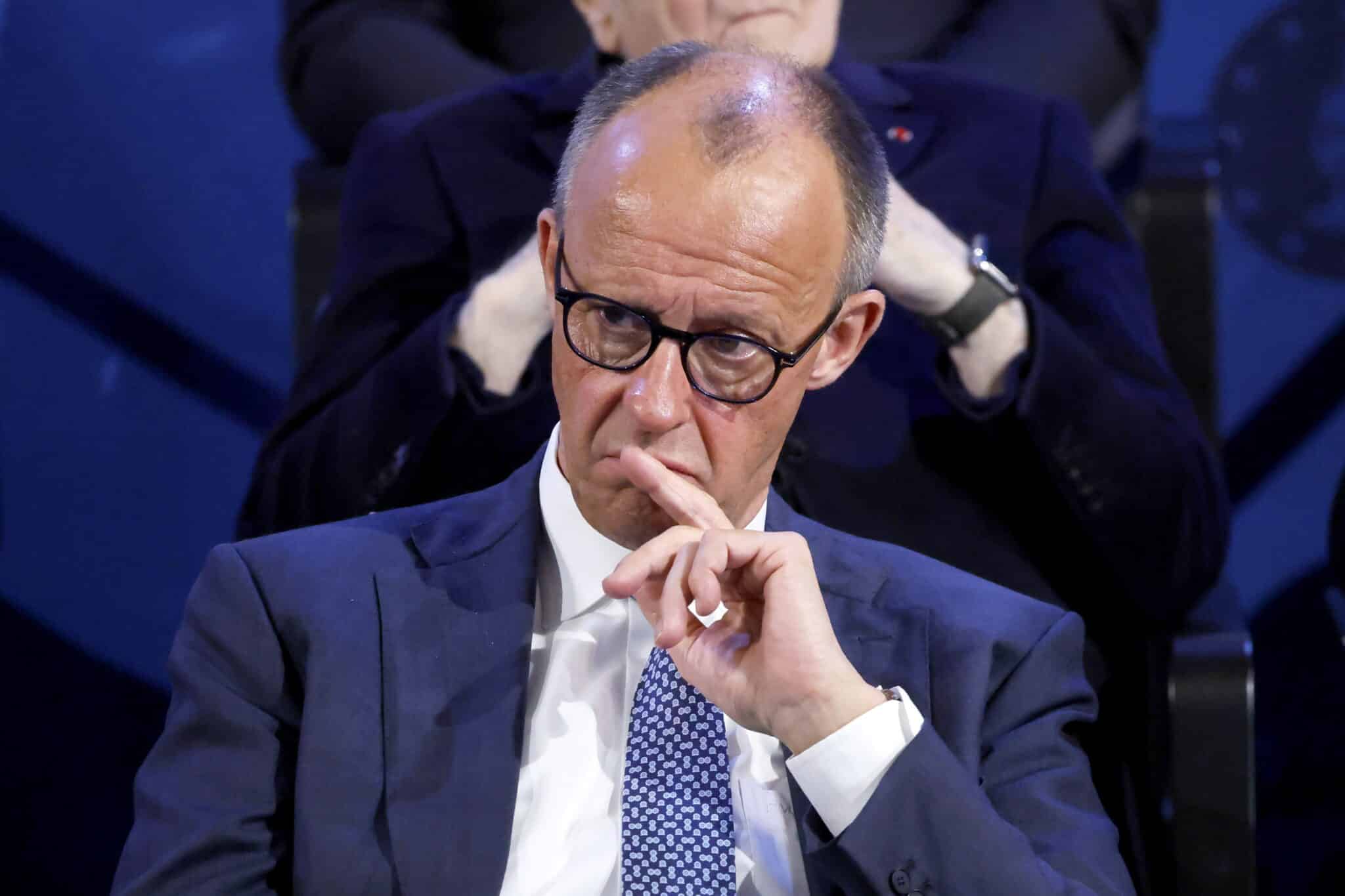 Friedrich Merz in Anzug, nachdenklich mit Hand am Kinn, sitzt im Publikum während der Karlspreisverleihung in Aachen.