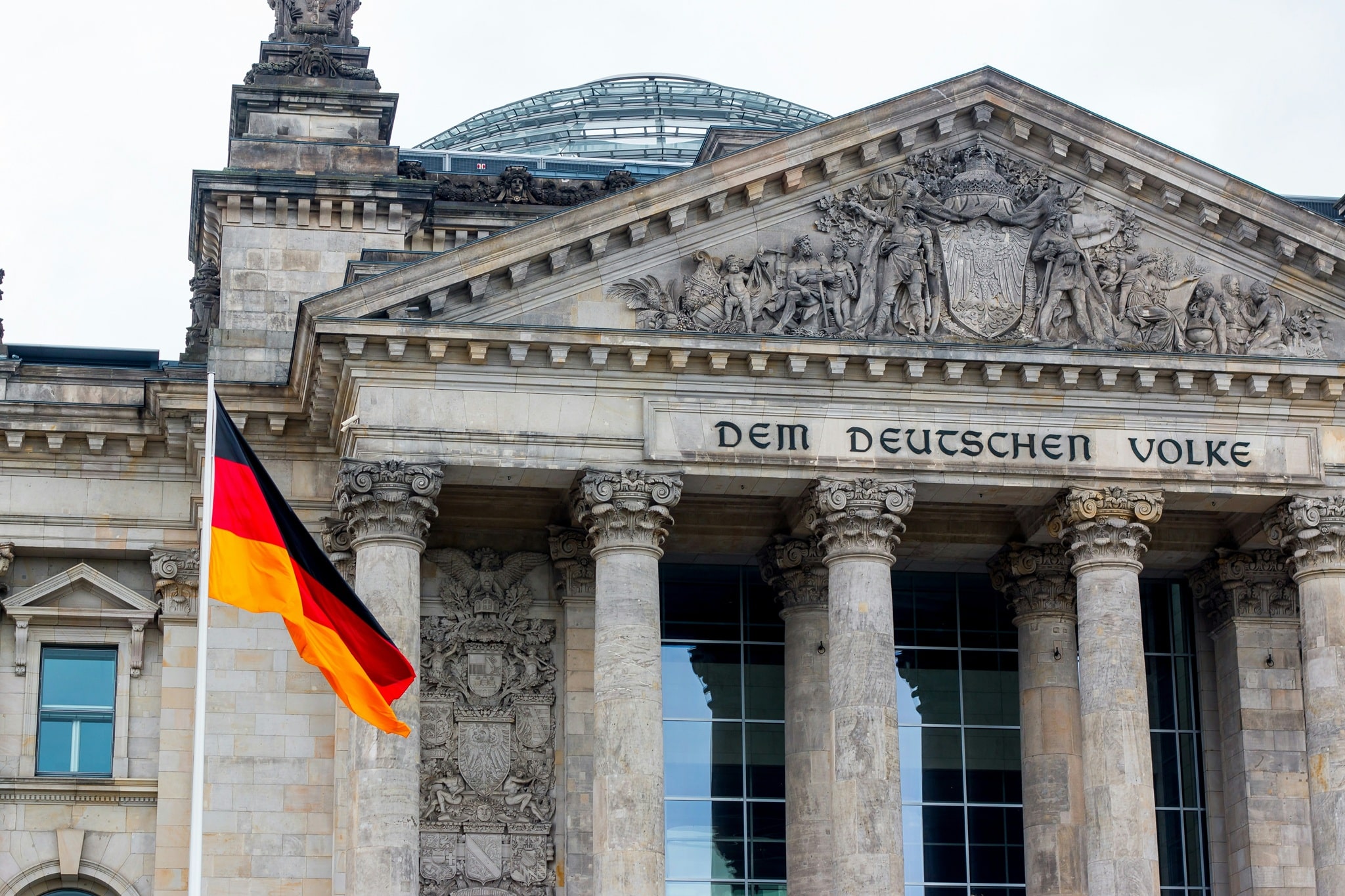 Reichstagsgebäude in Berlin mit deutscher Flagge und der Inschrift "DEM DEUTSCHEN VOLKE" über der Eingangstür.