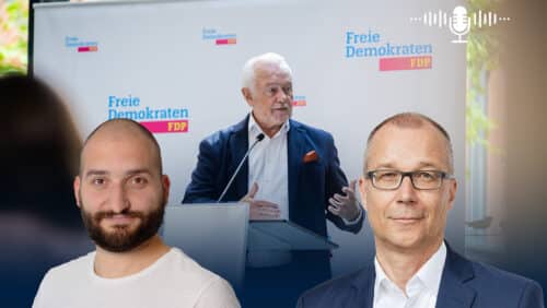 Mann spricht am Rednerpult vor einem Banner der Freien Demokraten, zwei Männer im Vordergrund.