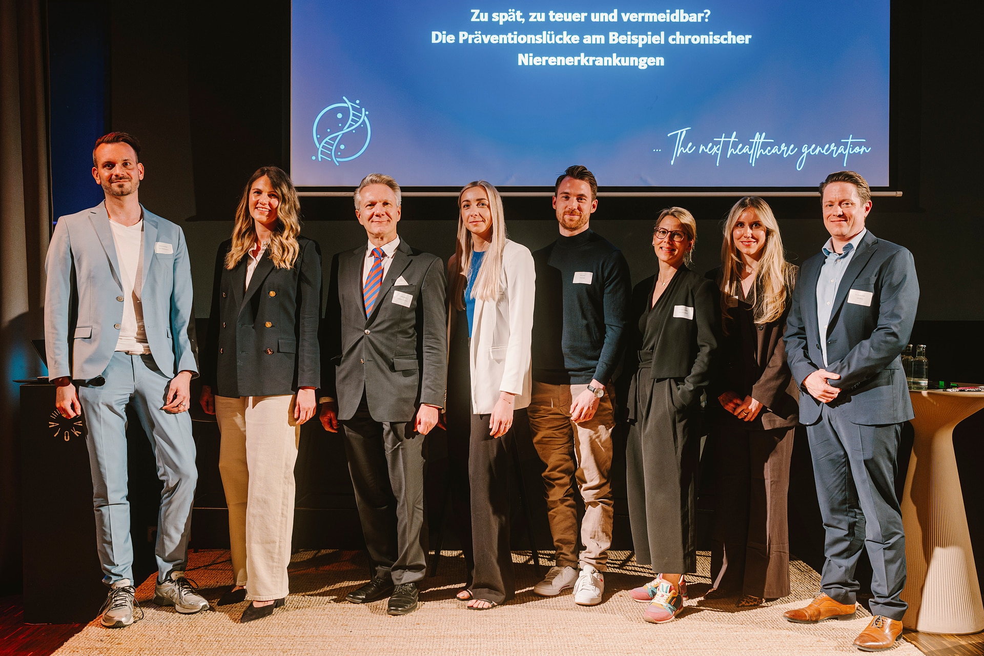 Gruppenfoto von acht Personen auf einer Bühne, die an einem Netzwerkabend über chronische Nierenerkrankungen teilnehmen.