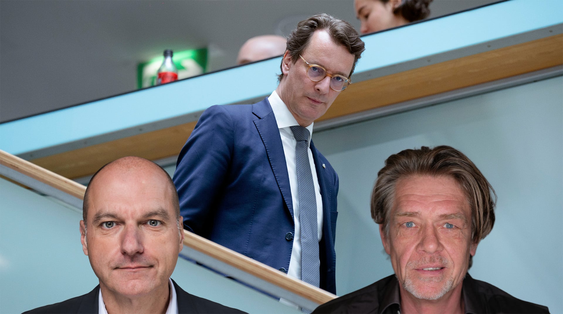 Mann in Anzug geht eine Treppe hinunter, zwei weitere Männer im Vordergrund, unscharf im Bild.