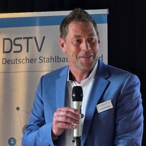 Mann mit Mikrofon in blauer Jacke spricht vor einem Banner des DSTV.