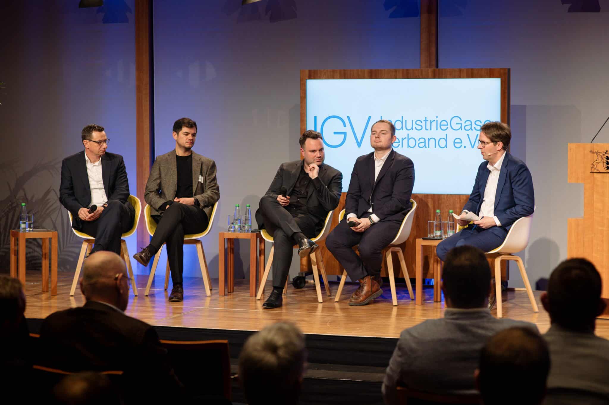 Podiumsdiskussion mit fünf Sprechern, die an einem Tisch sitzen, vor einem Banner des IGV im Hintergrund.
