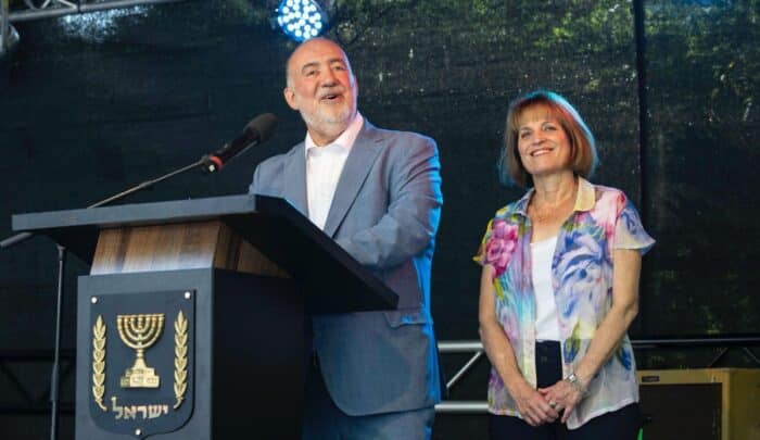 Mann und Frau stehen am Rednerpult, lächeln, während sie bei einem Sommerfest im Botschaftsgarten sprechen.