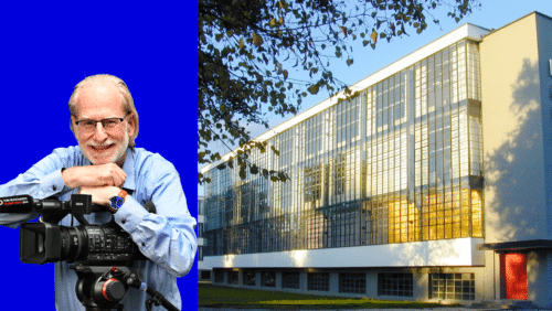 Ein älterer Mann mit Brille und Kamera lächelt vor dem Bauhaus-Gebäude mit großen Fenstern und einem roten Eingang.