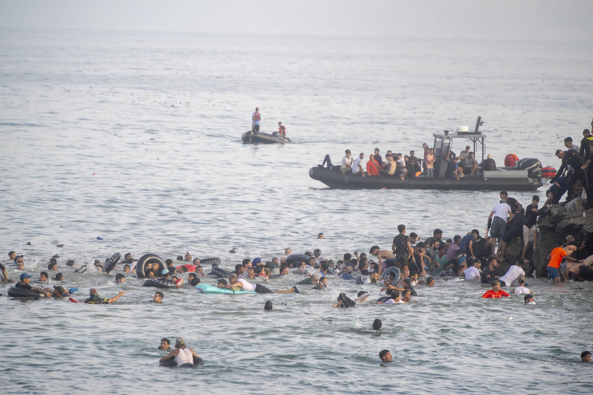Hunderte Migranten schwimmen in Ceuta, während Rettungsboote Menschen aus dem Wasser ziehen.