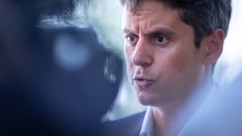 Mann mit dunklen Haaren spricht ernsthaft in ein Mikrofon, umgeben von Kameras und Journalisten.