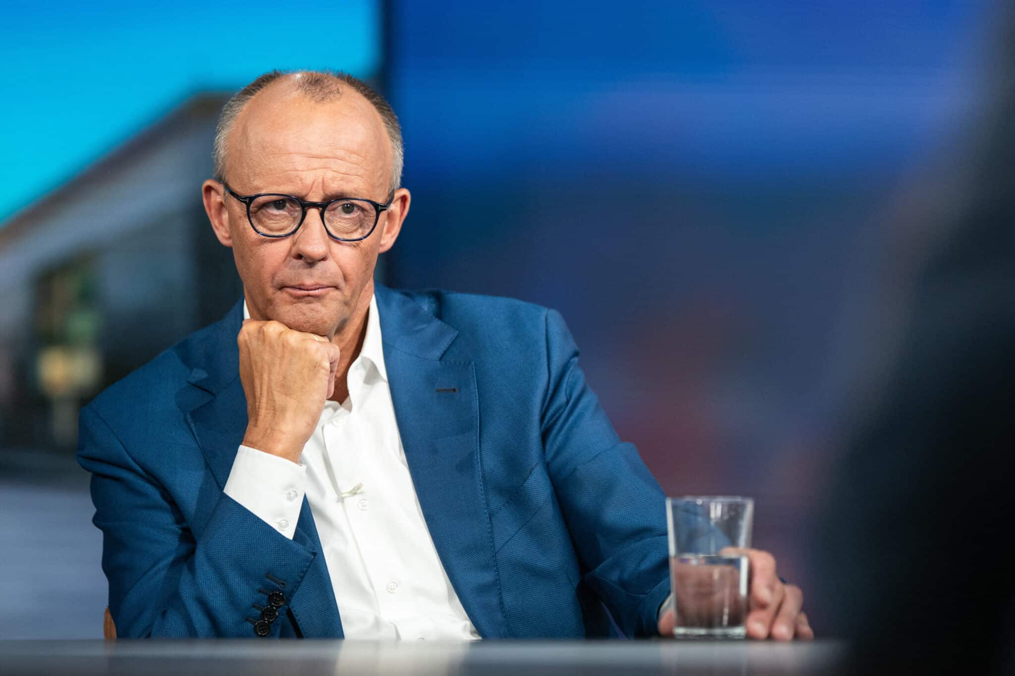 Bundeskanzler Friedrich Merz sitzt nach einem RTL-Interview mit einem Glas Wasser und hört einem Studiogast aufmerksam zu.