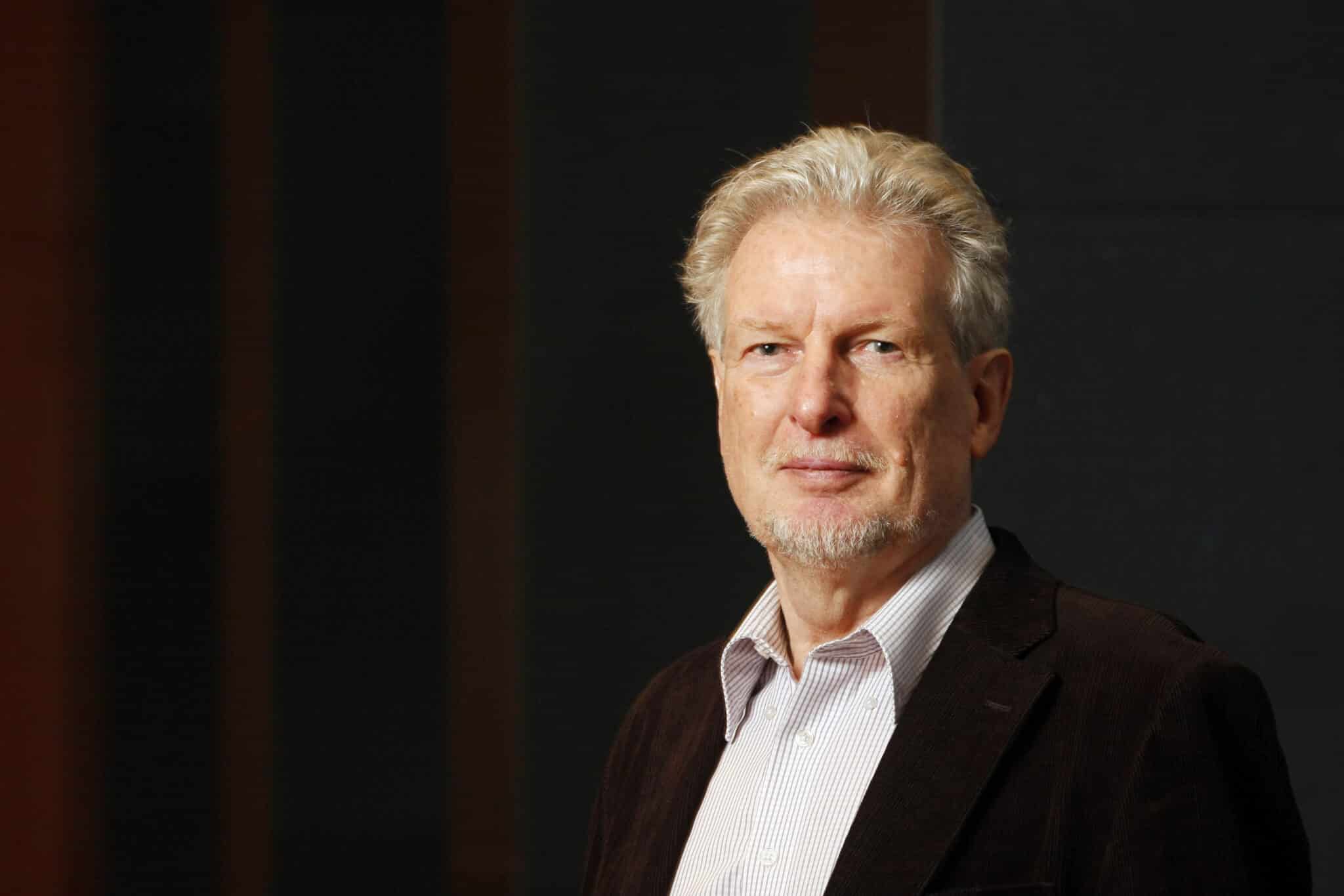Porträt von Peter Voss, lächelnd, mit grauen Haaren, in einem dunklen Sakko vor einem neutralen Hintergrund.